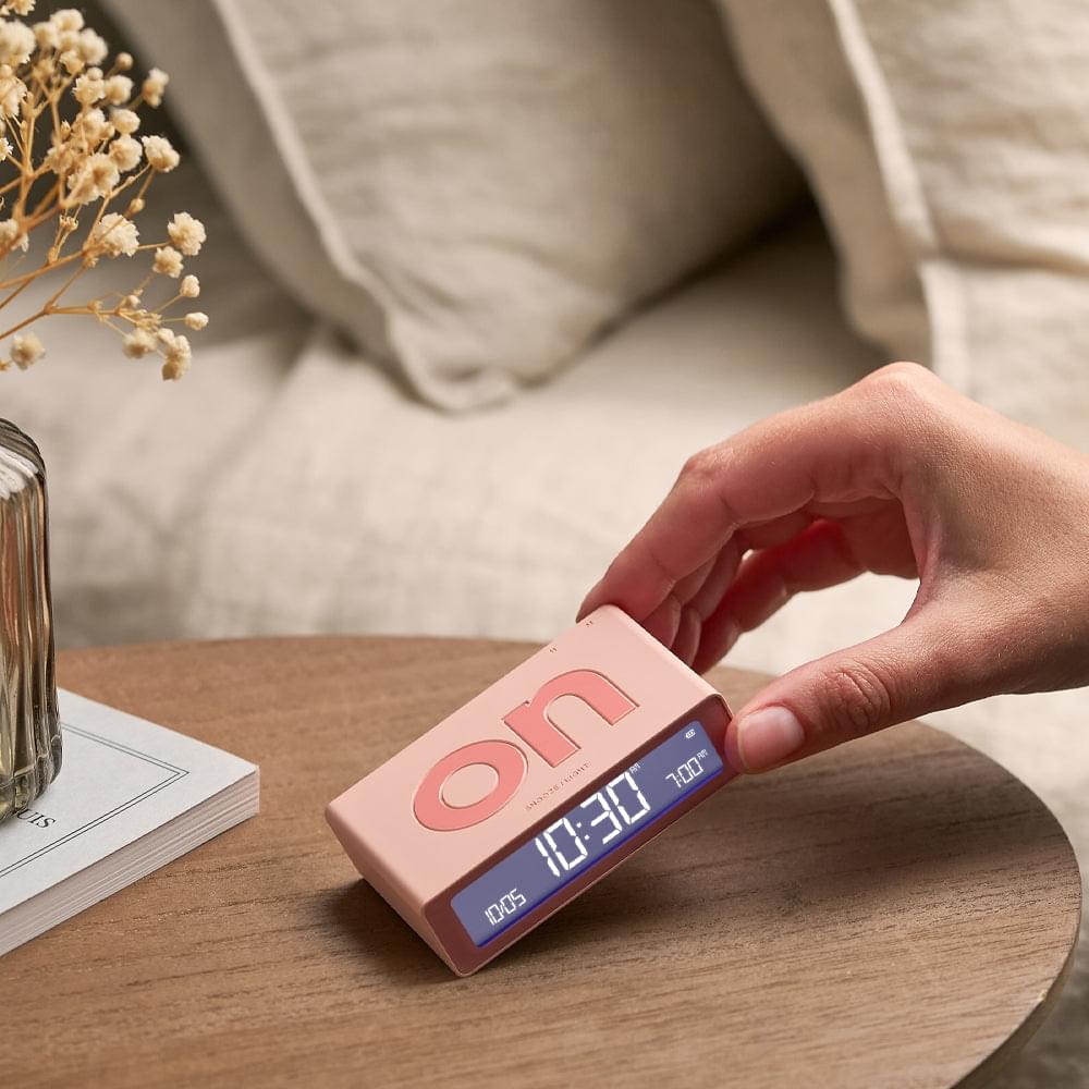Pink mini flip alarm clock held by hand, front LCD time display visible