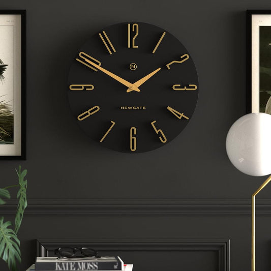 Round black Newgate wall clock with gold hands, large numerals, and center logo