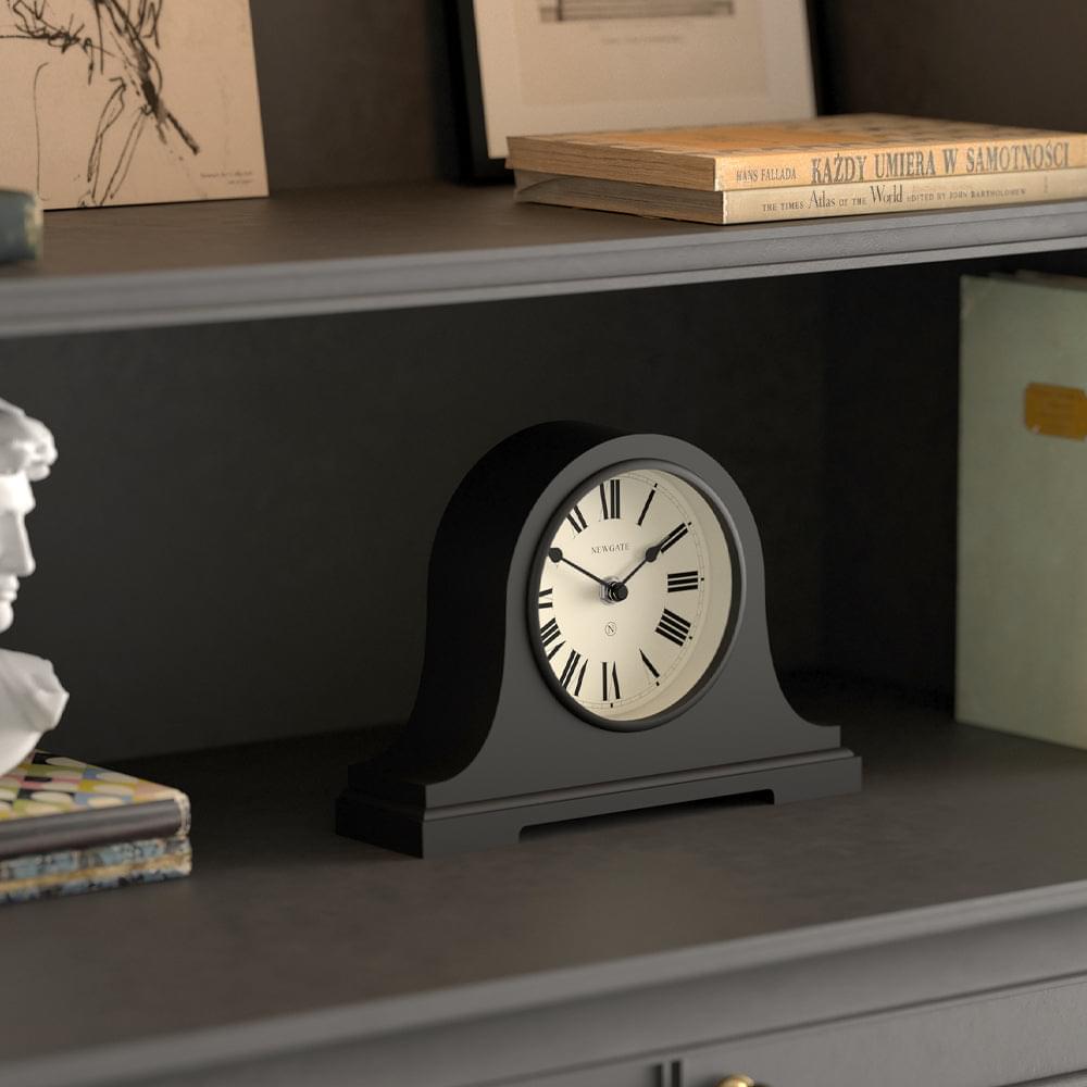 Black mantel clock with arched case and white dial displayed on a tabletop shelf