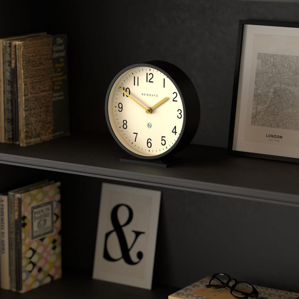 Black mantel clock with cream dial and gold hands, standing on a shelf