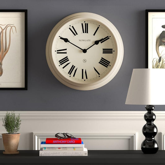 Vanilla cream wall clock on interior wall, Roman numerals and black hands