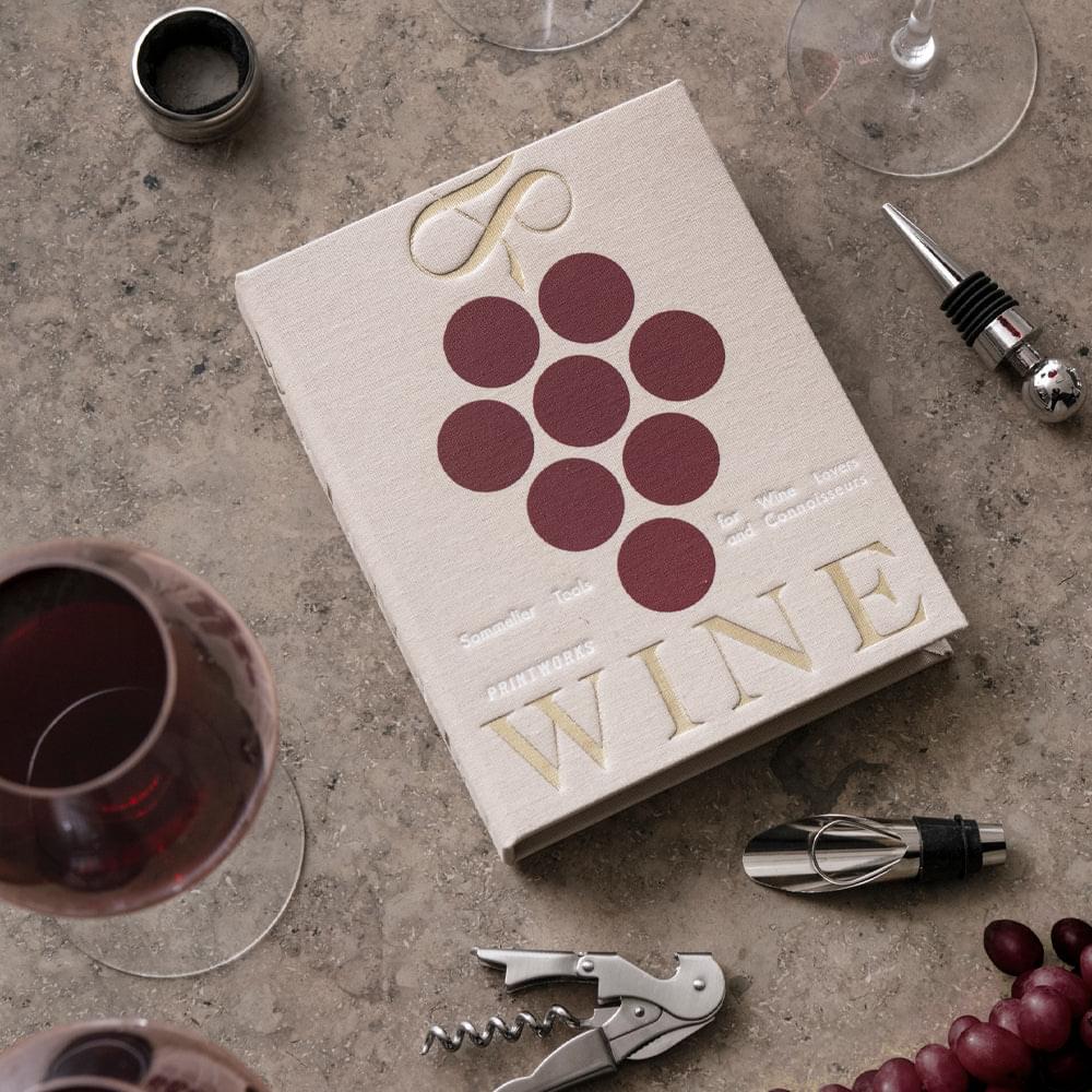 Beige wine tools box with wine-themed cover, with corkscrew and stoppers nearby