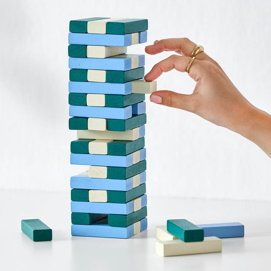 Tumbling tower game with stacked teal and blue blocks; hand removing a top block