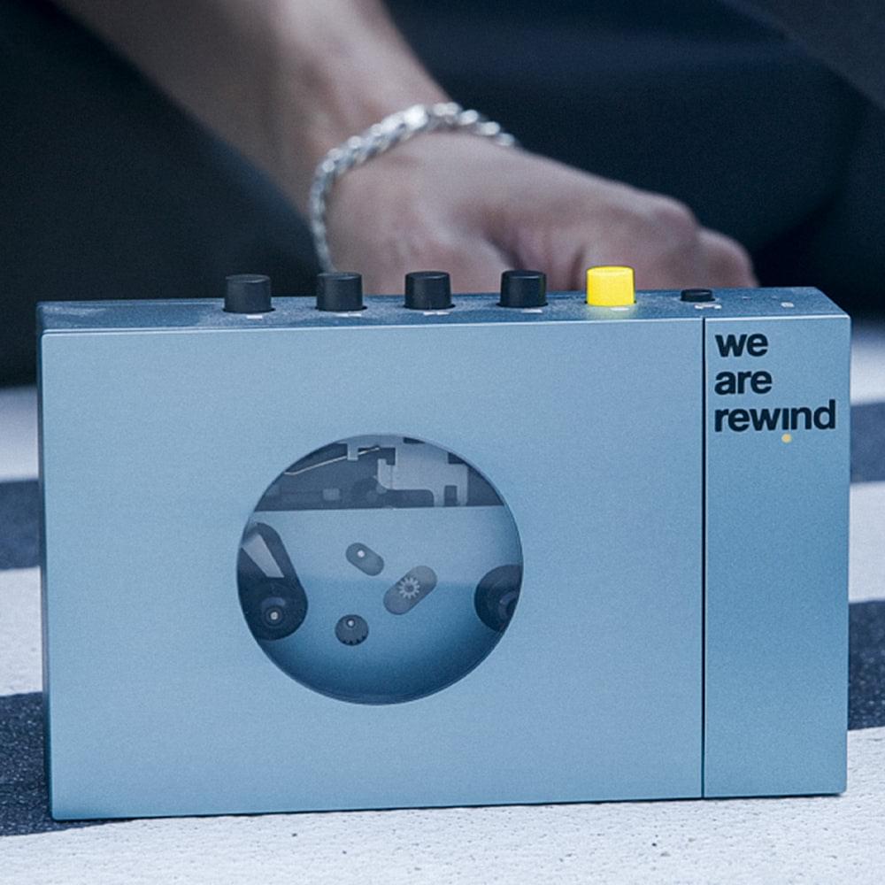 Blue portable cassette player on tabletop with top knobs and “we are rewind” logo