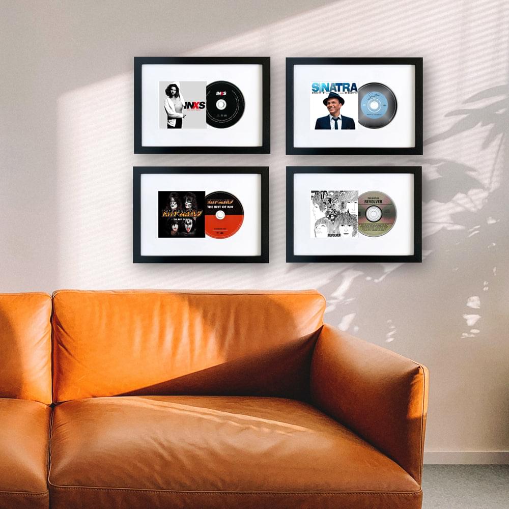 Four black-framed album art displays on wall above orange sofa