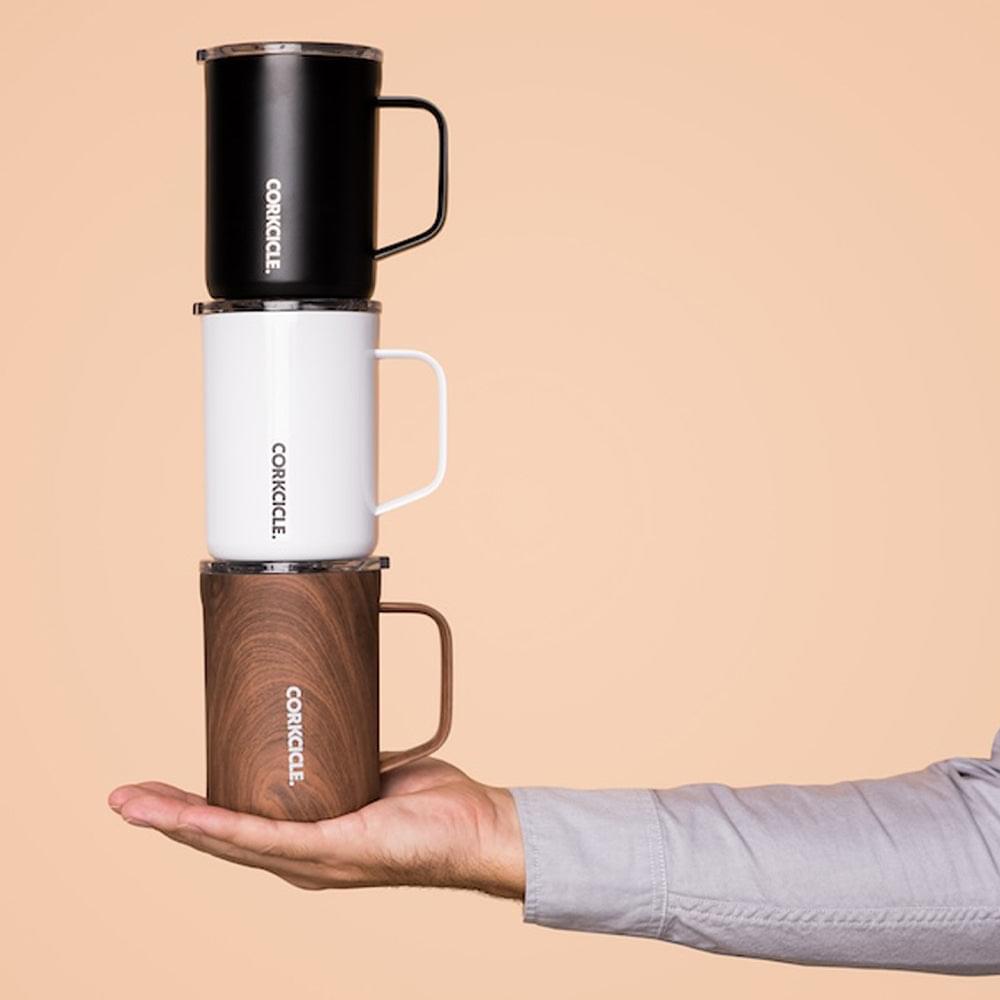 Stacked insulated mugs: matte black with handle and clear lid, held in hand