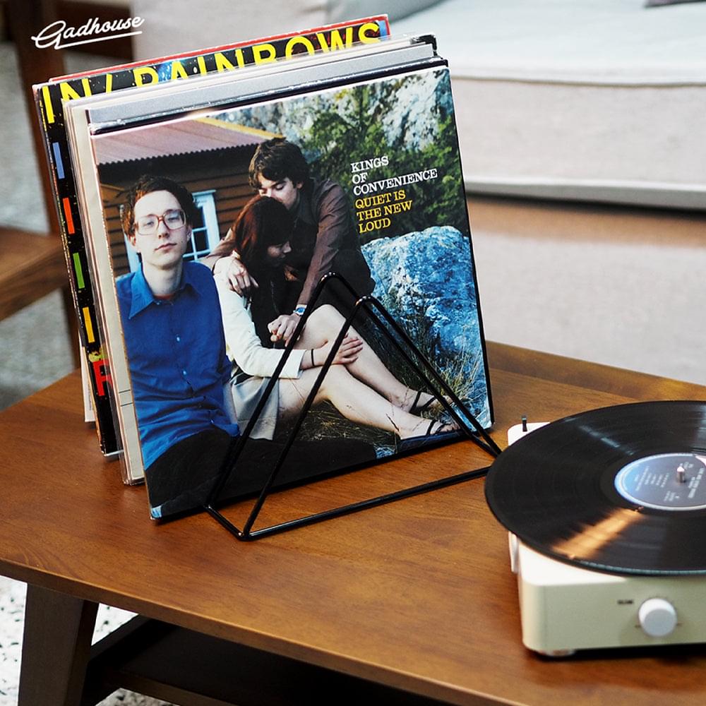 Black wire vinyl record rack holding upright records; portable turntable nearby