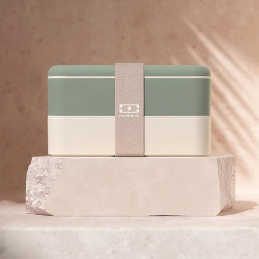 Sage green and white bento box with beige strap on a foil base