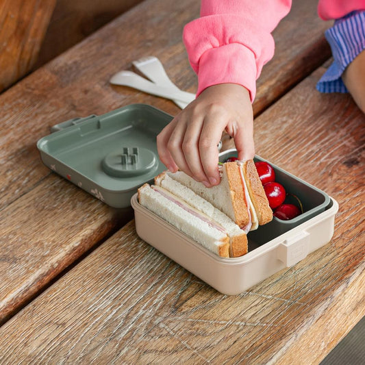 Snack lunch box on table with sandwich slices and cherry tomatoes inside, child hands