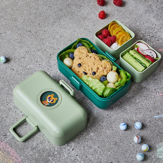 Open green kids bento lunch box with compartments filled with salad, fruit, and crackers.
