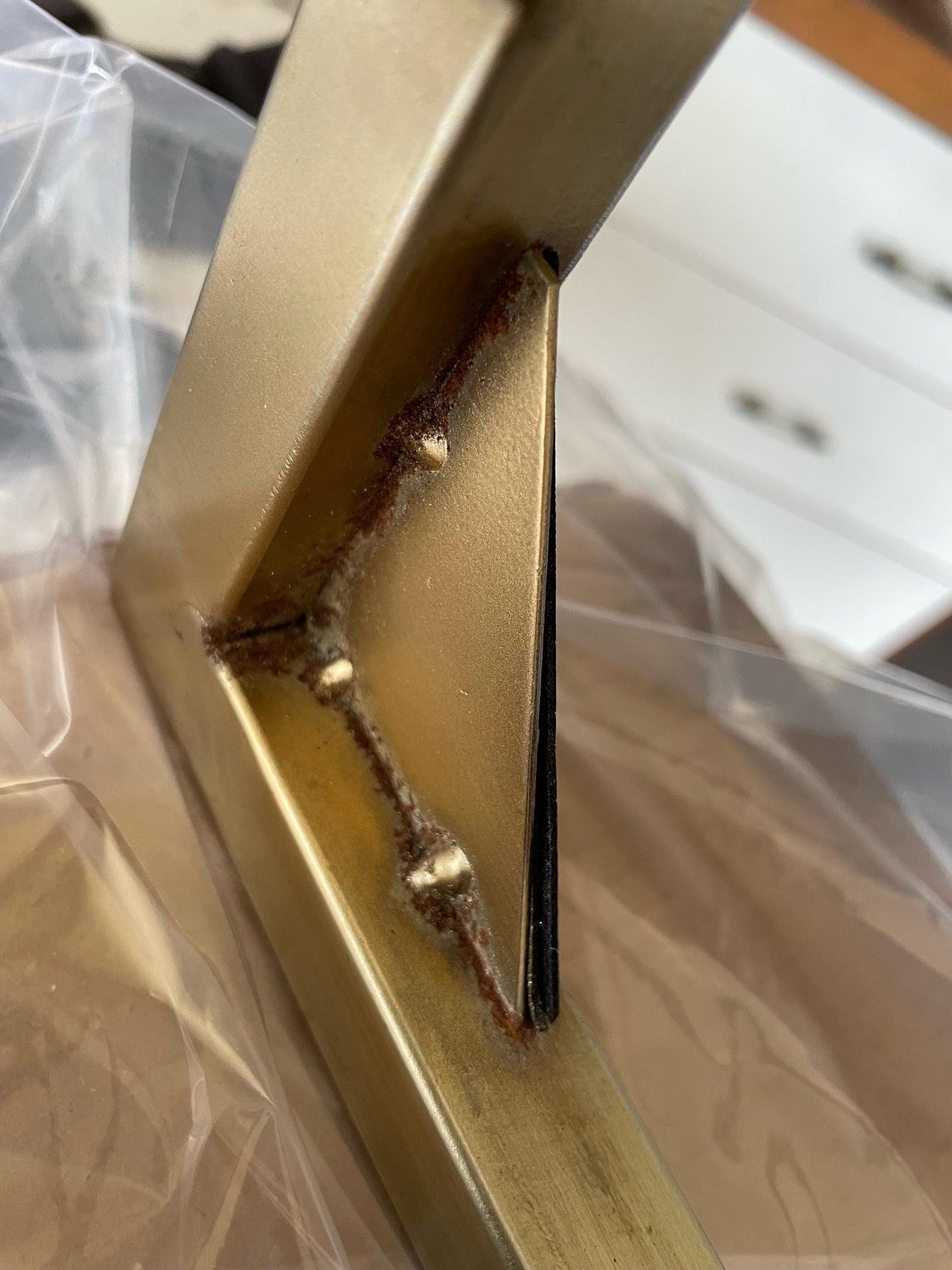 Close-up of gold-toned frame weld and corner on a glass-top side table