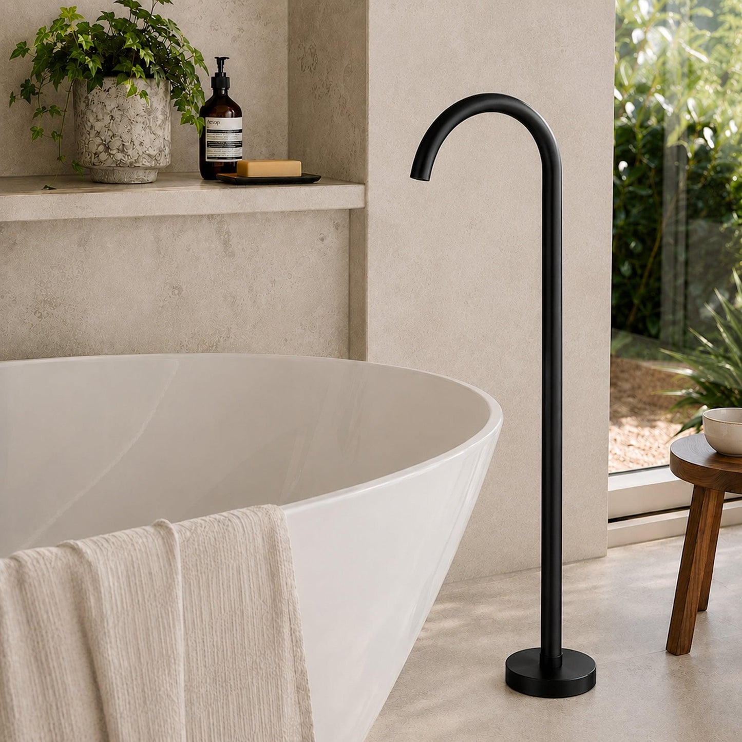Matt black freestanding bath spout beside oval freestanding bath and round base