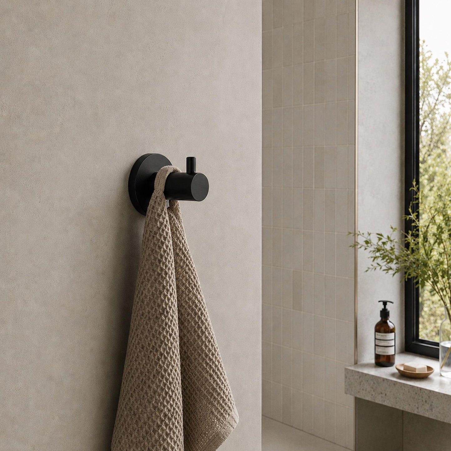 Matte black wall-mounted robe hook with round plate, holding a hanging towel