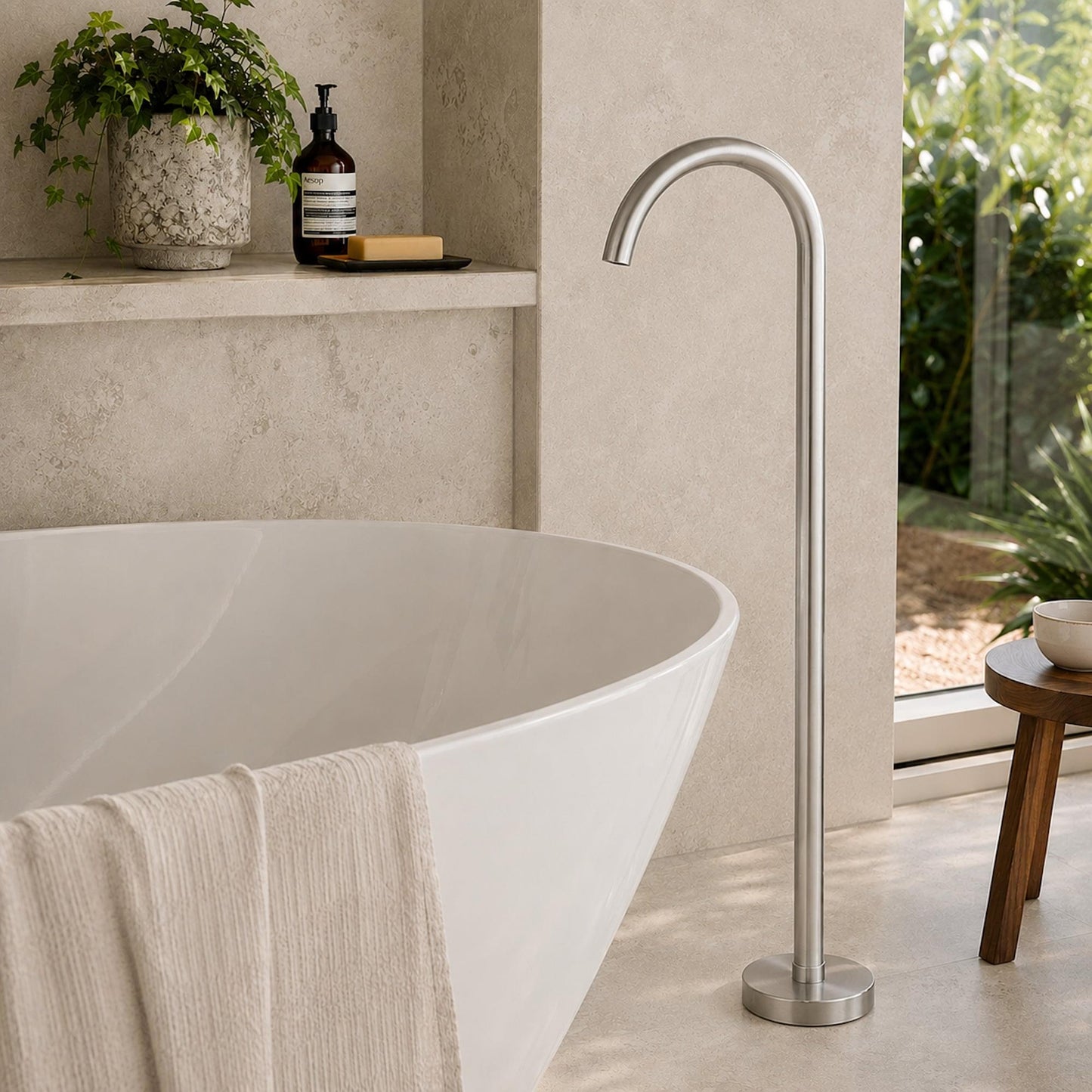 Freestanding bath spout, brushed nickel finish, curved spout standing by a bathtub.