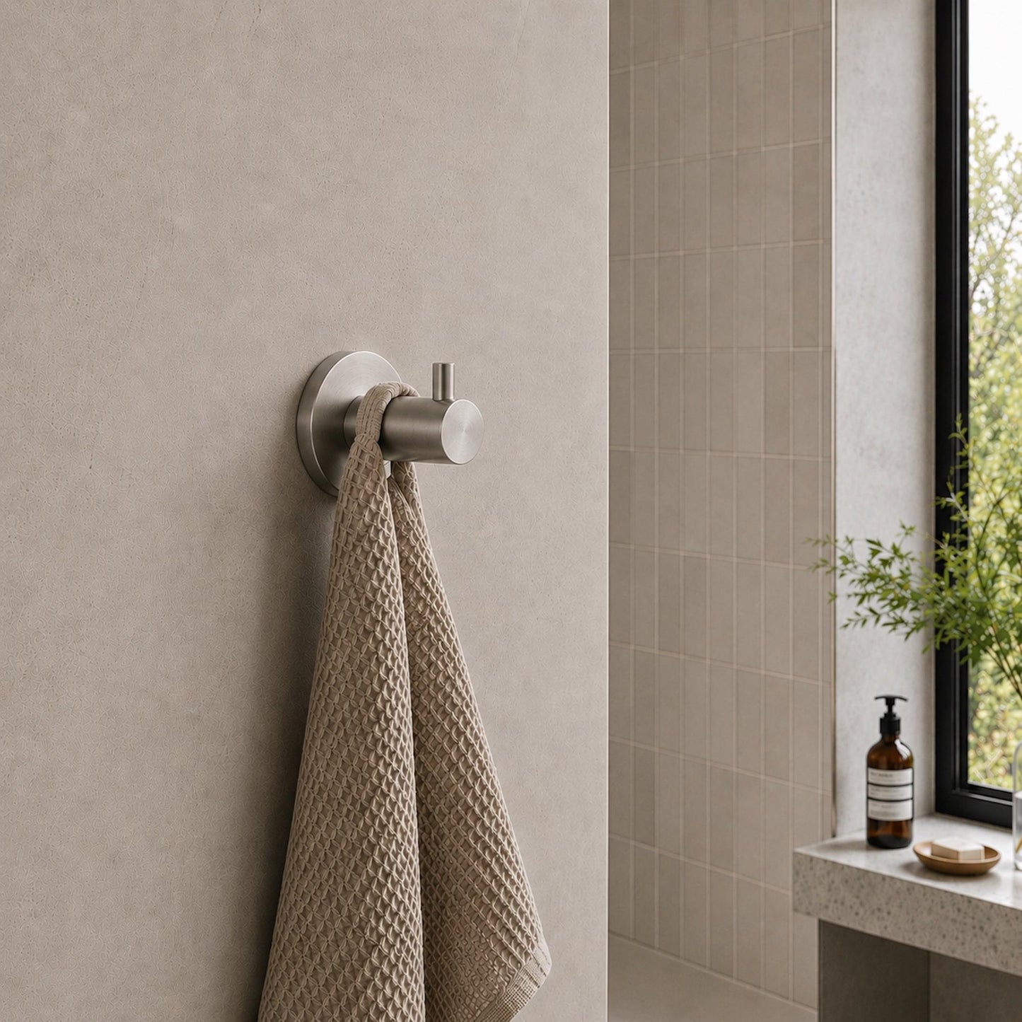Brushed nickel robe hook holding a textured beige towel on wall