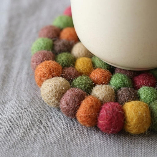 Round wool felt coaster with dense multicolor pom-pom edge under mug
