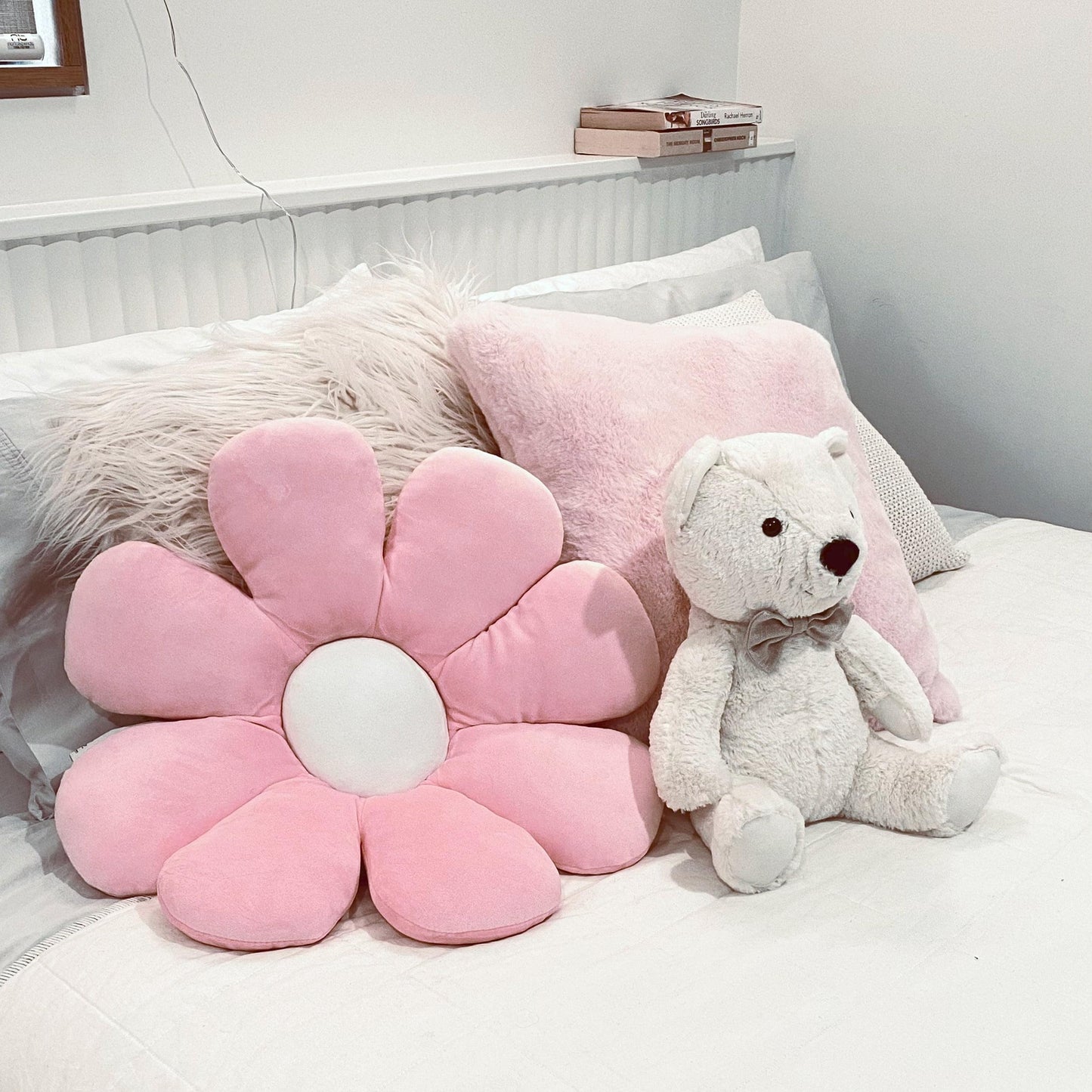 Pink daisy-shaped plush pillow with white center cushion on a bed