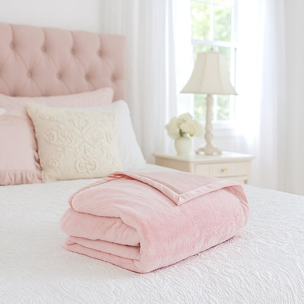 Pink plush fur throw blanket folded on a bed, showing thick soft texture