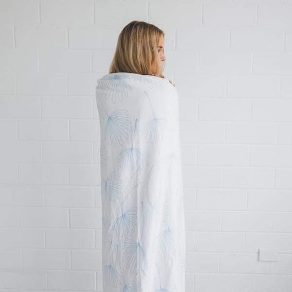 Round white beach blanket with light-blue dandelion print and fringed edge, worn as shawl