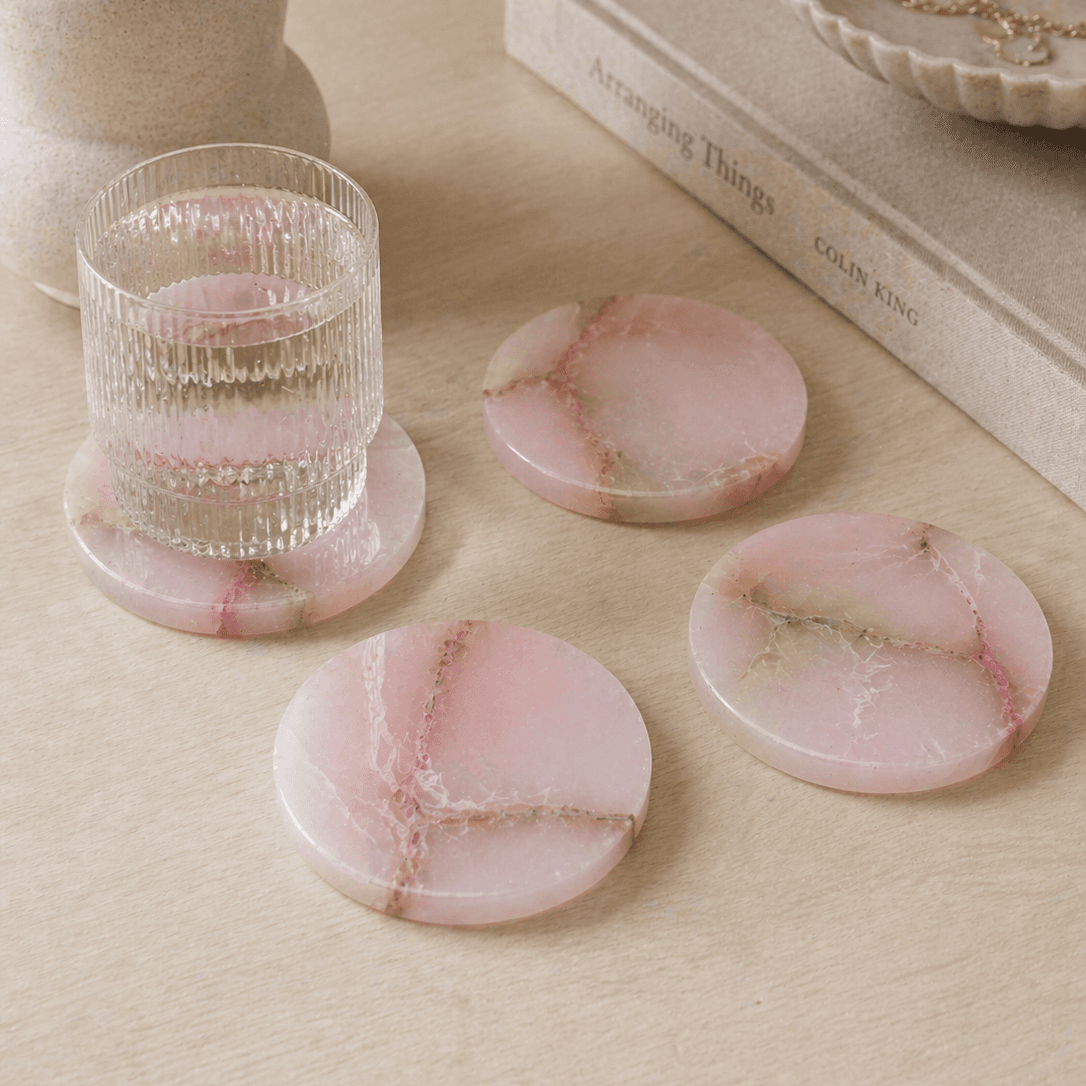 Round pink alabaster coasters with natural veining, four-piece set on wood surface