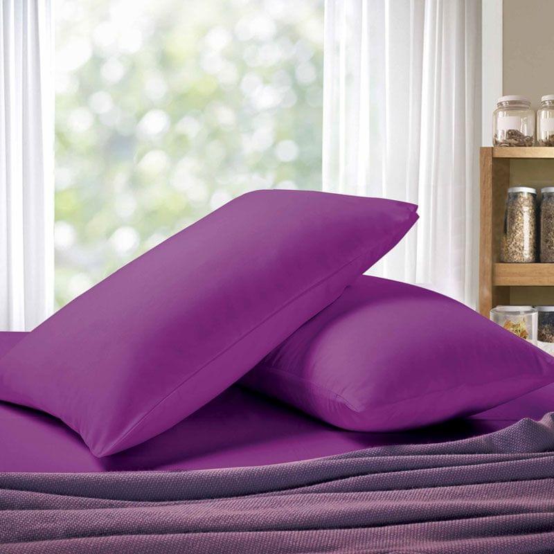 Purple king pillowcases, one pillowcase and one pillow pile on bed