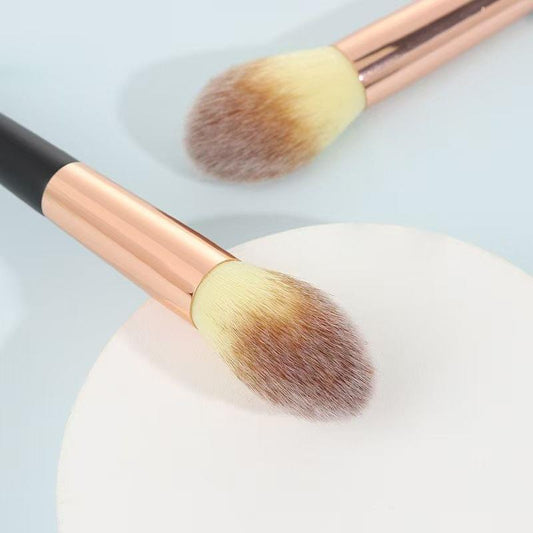 Cosmetic powder brush head close-up; rounded bristles on rose-gold sleeve, black handle