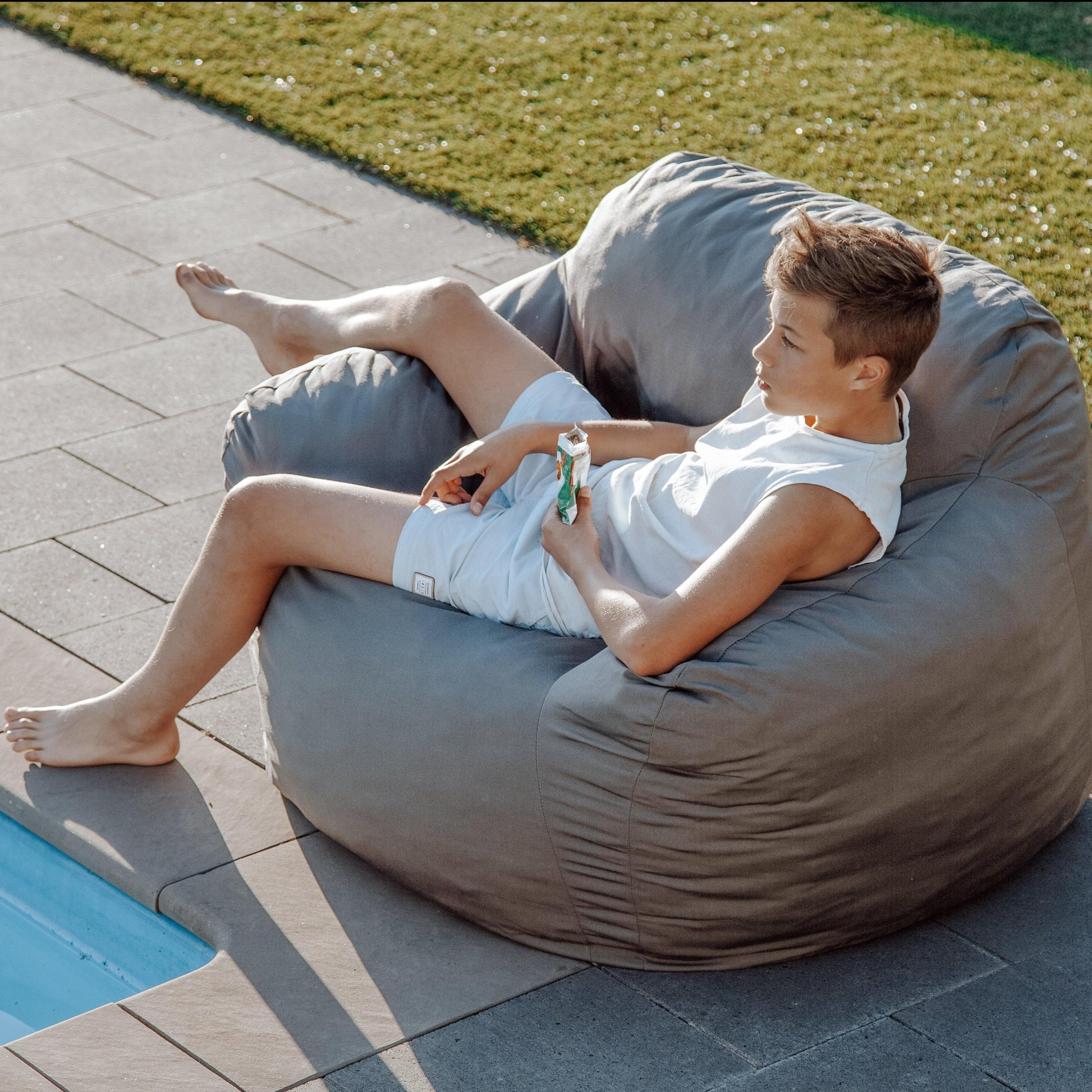 Charcoal grey outdoor bean bag chair, shown being lounged on