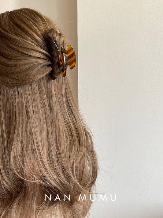 Large acetate hair claw clip with dark amber tortoiseshell stripes, clamped on hair.