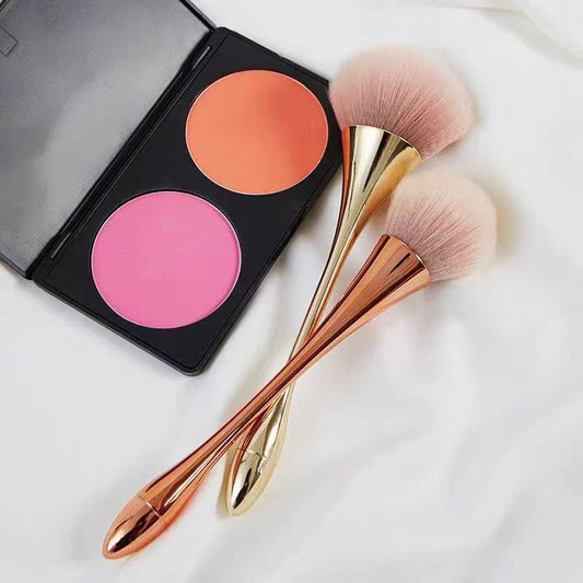 Rose gold powder brush trio with fluffy pink heads beside blush compact