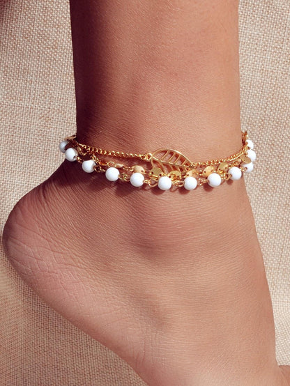 Gold-tone anklet on ankle with white beads and leaf charm, layered chain design