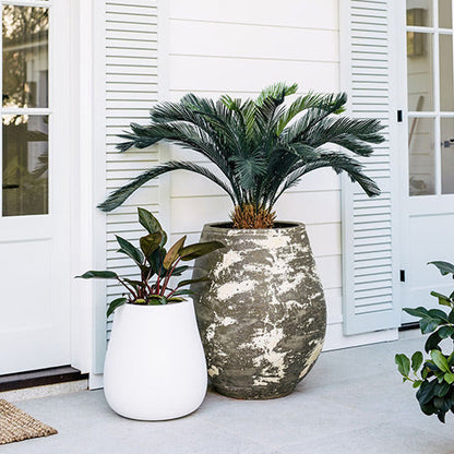 Large speckled ceramic planter pot with palm fronds beside small white planter