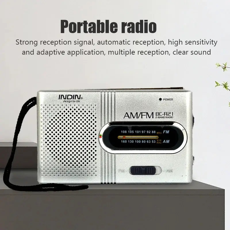 Compact silver AM/FM radio on tabletop, speaker grille and tuning dial with bands displayed.