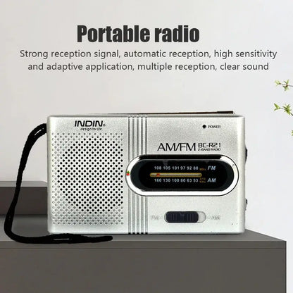 Compact silver AM/FM radio on tabletop, speaker grille and tuning dial with bands displayed.
