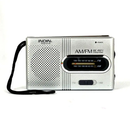 Silver AM/FM portable radio with speaker grille and tuning dial, black shoulder strap.