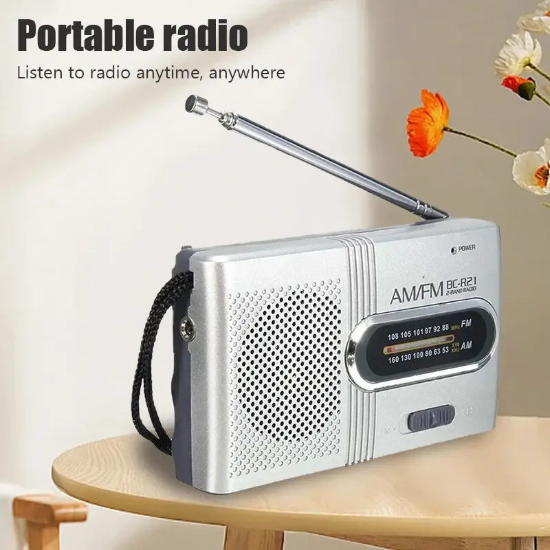 Silver AM/FM portable radio with built-in speaker grille, tuning dial and long antenna.