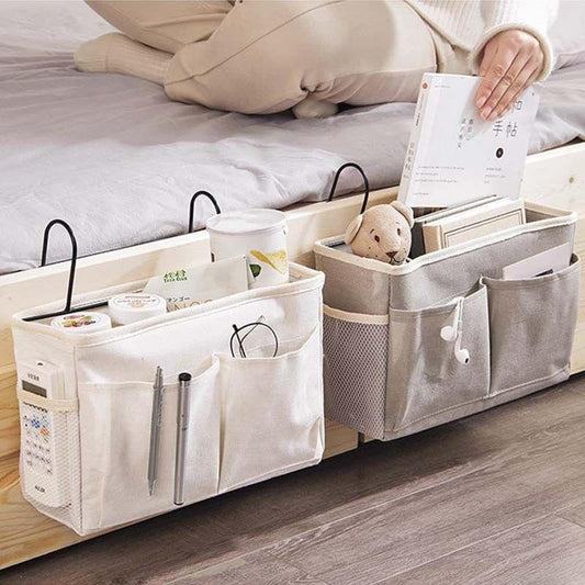 Multi-pocket hanging bed caddy with metal handles on a sofa beside linens