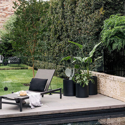 Charcoal cylindrical planter pots with leafy plants on a patio