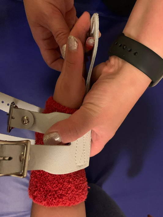 Close-up of uneven bar gymnastics grips: white strap with metal buckle holes