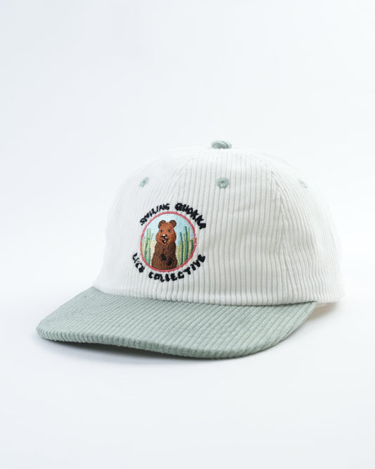 White ribbed baseball cap with circular quokka patch and light gray curved brim.
