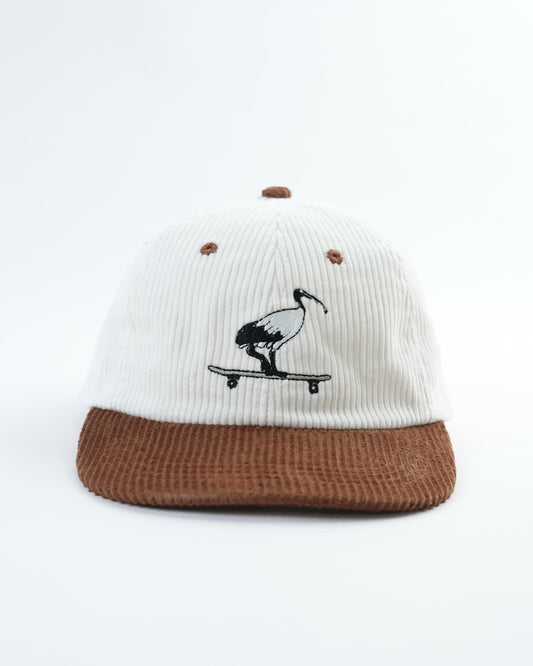 White cap with brown brim, black bird-on-skateboard graphic, small stud details