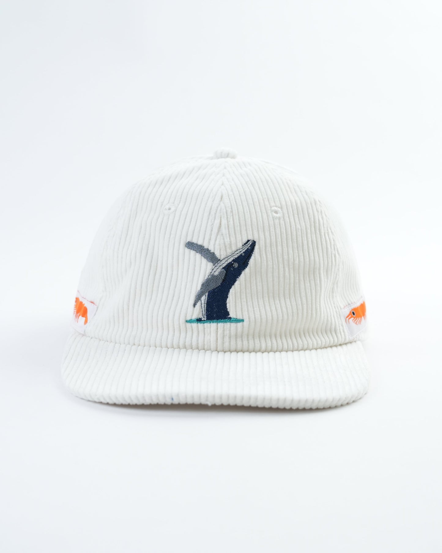 White cap with embroidered whale graphic and small orange fish patches