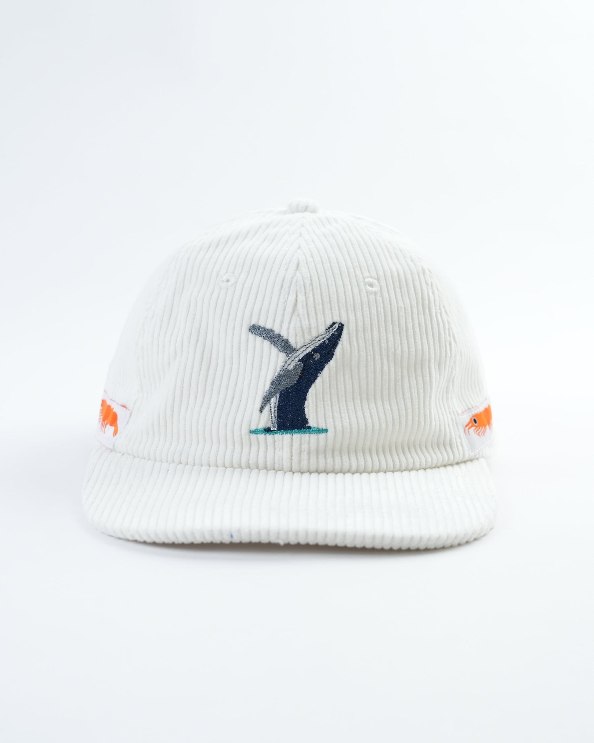 White cap with embroidered whale graphic and small orange fish patches