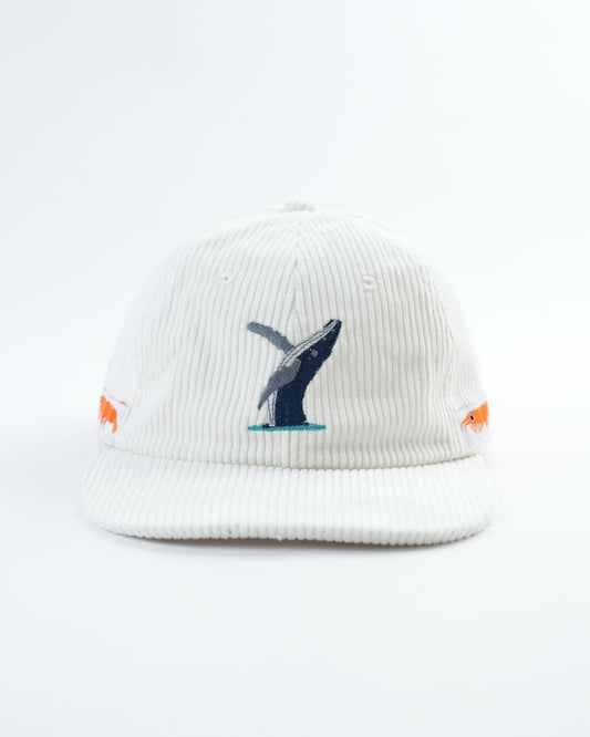 White cap with embroidered whale graphic and small orange fish patches