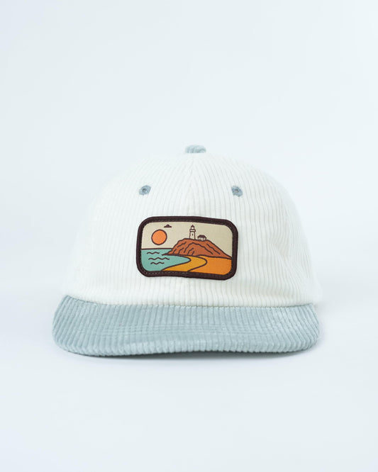 White corduroy baseball cap with light blue brim and framed beach scene front patch
