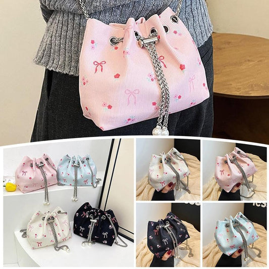 Pink drawstring mini bucket bag with bow print and silver chain strap, worn on model