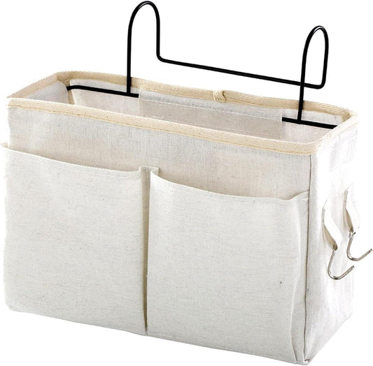 Off-white canvas hanging bed organizer bag with two metal hooks and four front pockets.