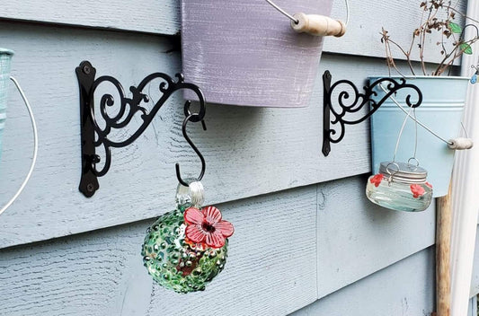 Black metal wall bracket with scroll design holding a hanging flower pot