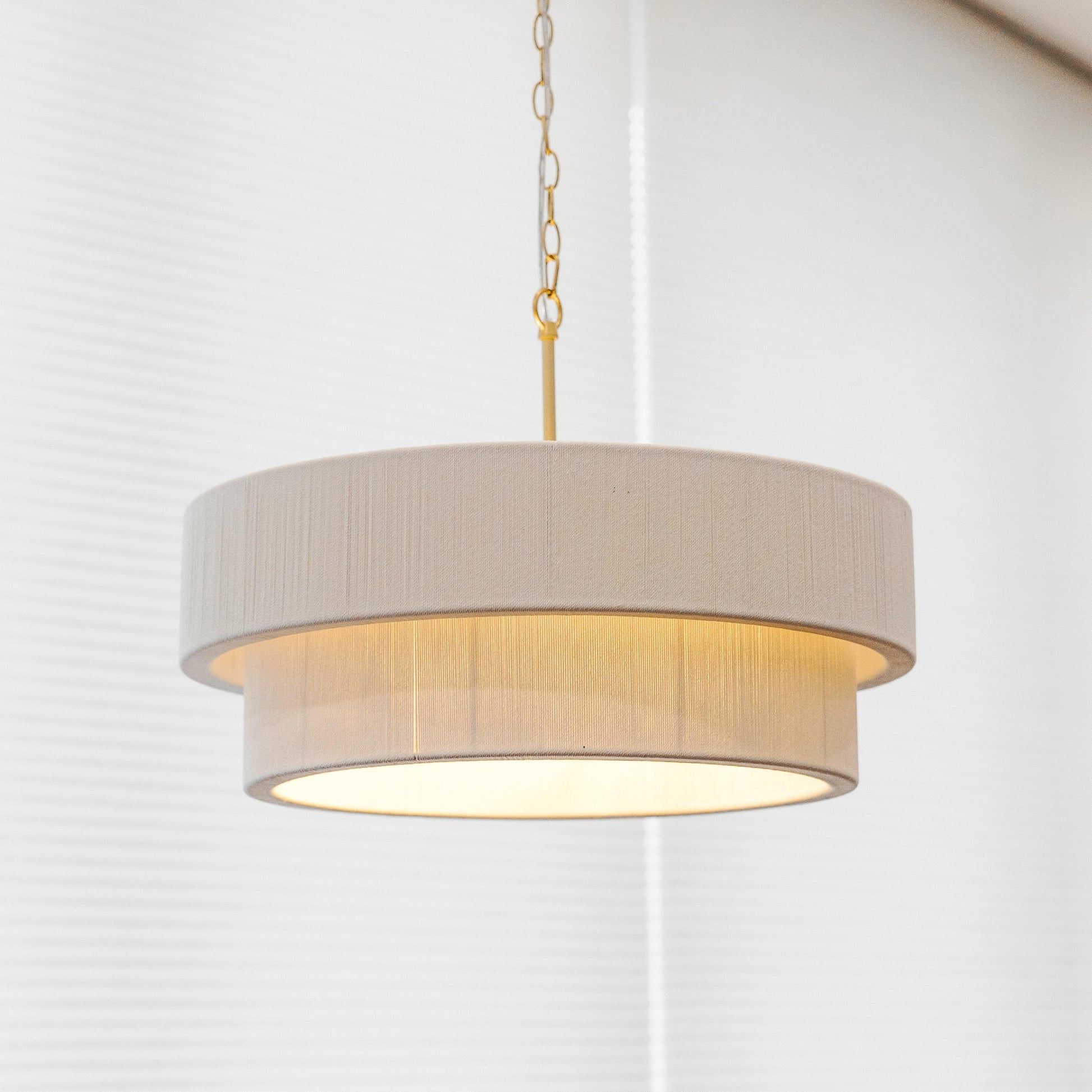 White linen double-tier chandelier shade with gold rope chain and warm light