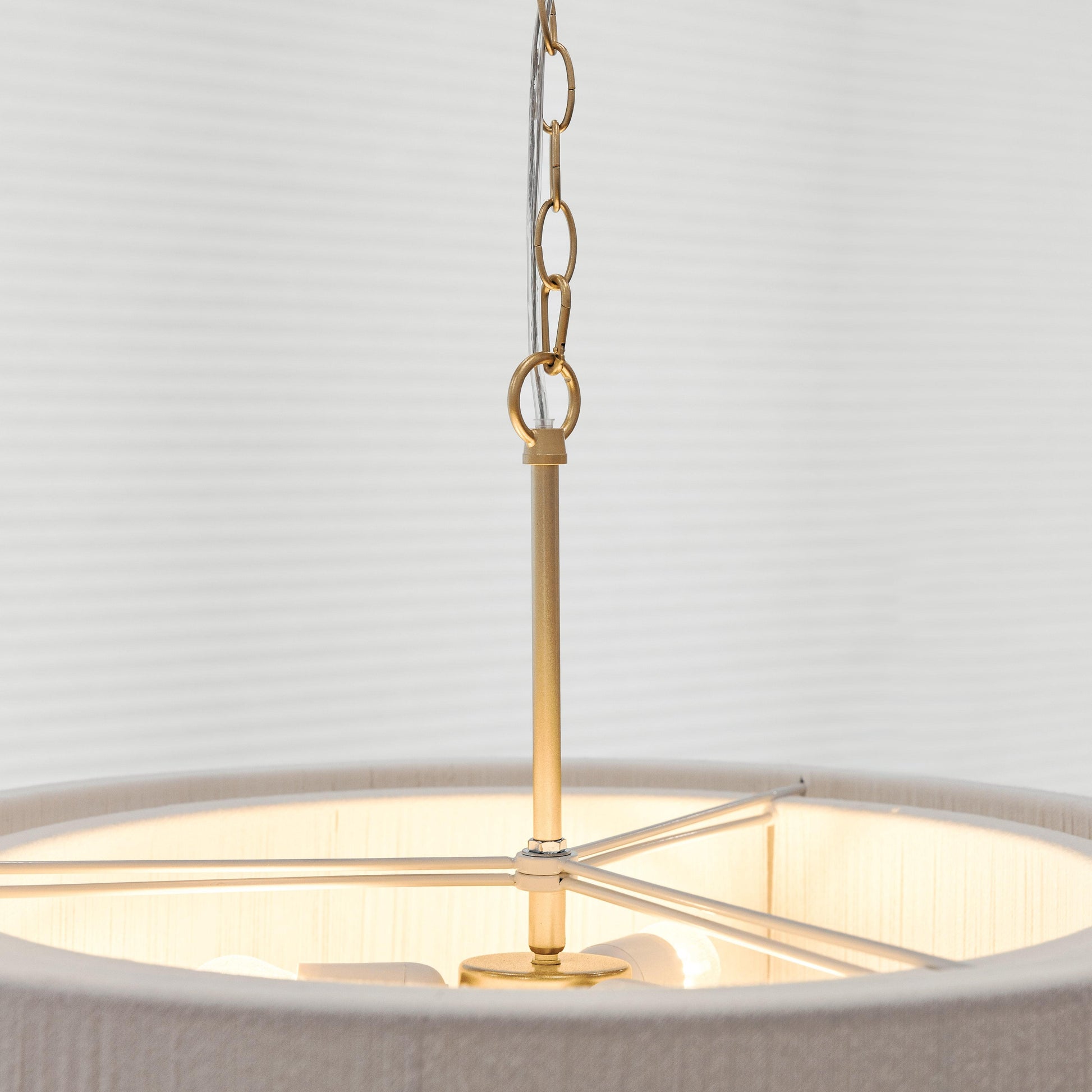 Gold chandelier mounting stem with rope chain over a white drum shade