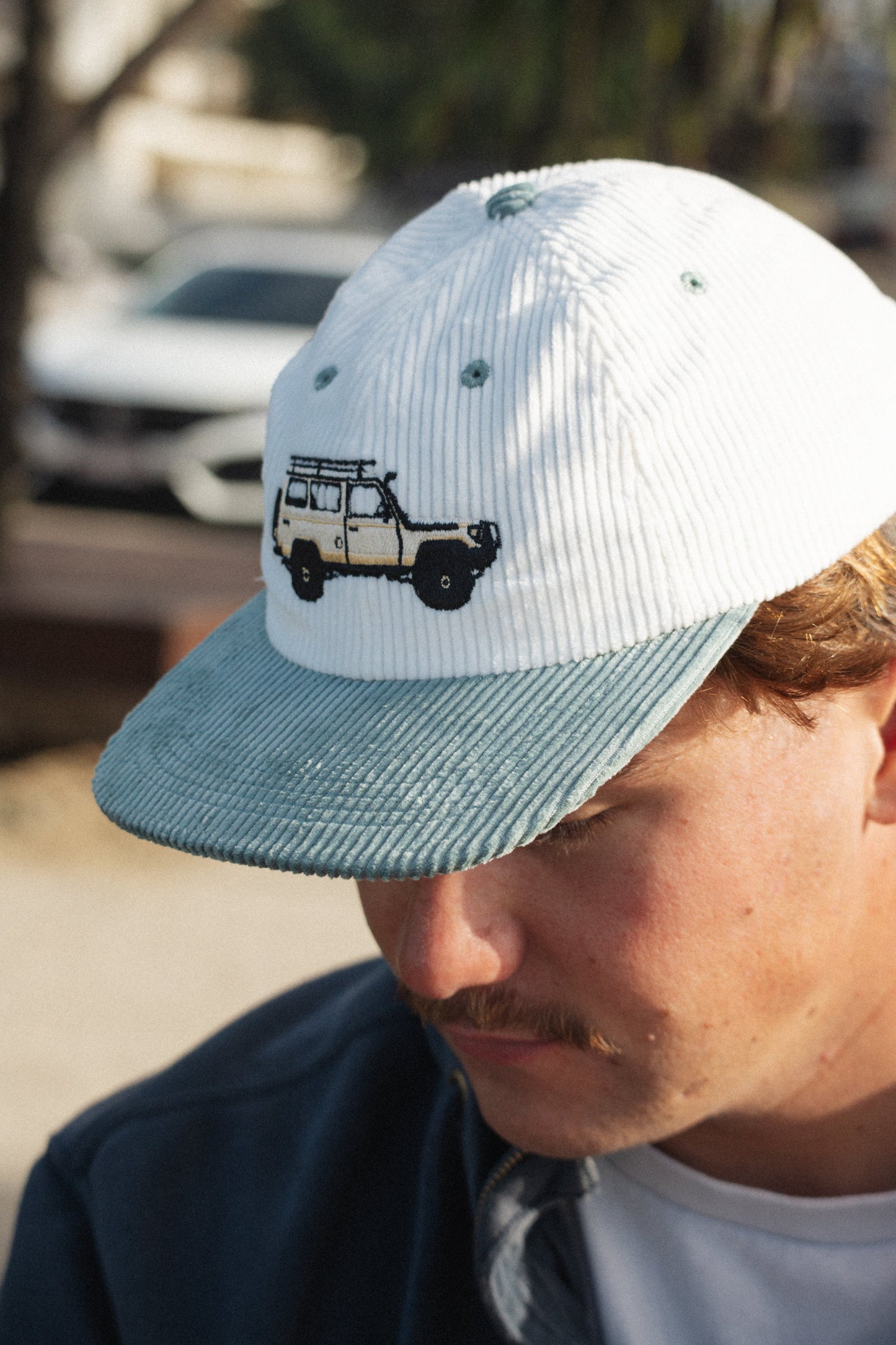 Troopy hat side view in white knit with teal brim and embroidered truck.